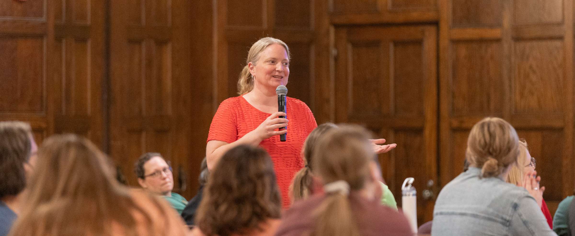 A women standing with a microphone giving a presentation. Several training attendees are in the foreground.