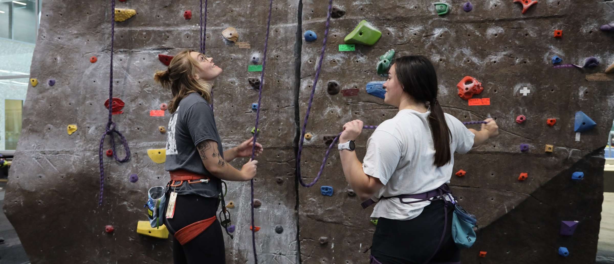 Two women standing at the base of the climbing wall at State Gym