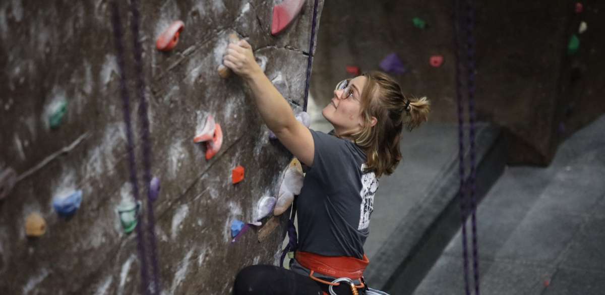 A women reaching for a hold on the State Gym climbing wall